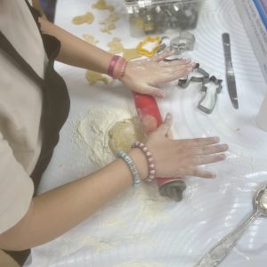 Un enfant est en train d'aplatir la pâte sablée avec un rouleau pour faire des mini-tartelettes.